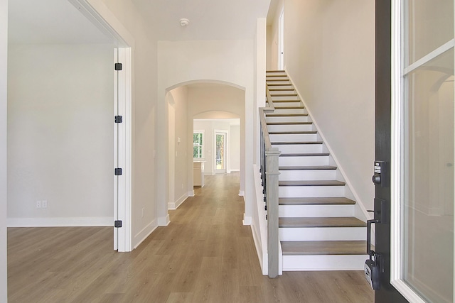 entryway with baseboards, stairs, arched walkways, and wood finished floors