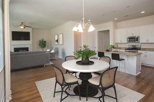 dining space with a fireplace, ceiling fan with notable chandelier, dark wood finished floors, and recessed lighting