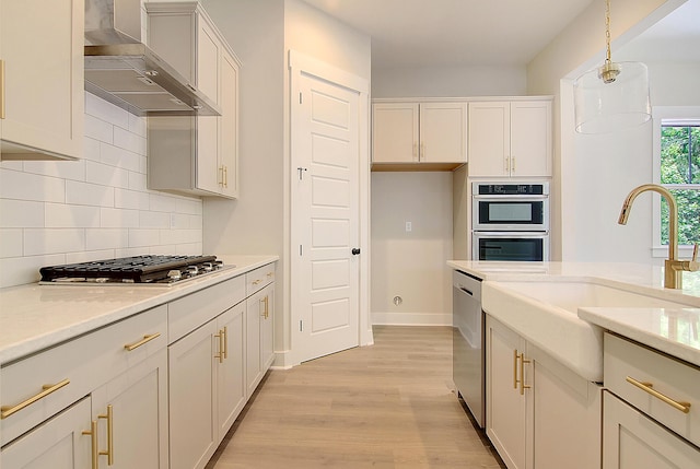 kitchen featuring stainless steel appliances, backsplash, decorative light fixtures, light wood-type flooring, and wall chimney range hood