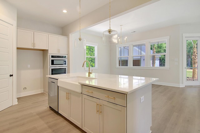 kitchen with white cabinetry, sink, hanging light fixtures, and a kitchen island with sink