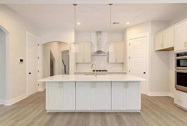 kitchen with arched walkways, light countertops, wall chimney range hood, and decorative backsplash