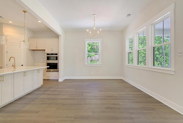 kitchen featuring an inviting chandelier, stainless steel double oven, wood-type flooring, pendant lighting, and white cabinets