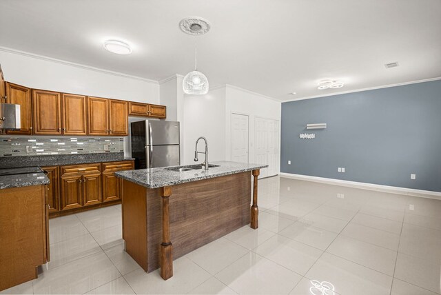 kitchen with an island with sink, stainless steel fridge, sink, tasteful backsplash, and dark stone counters