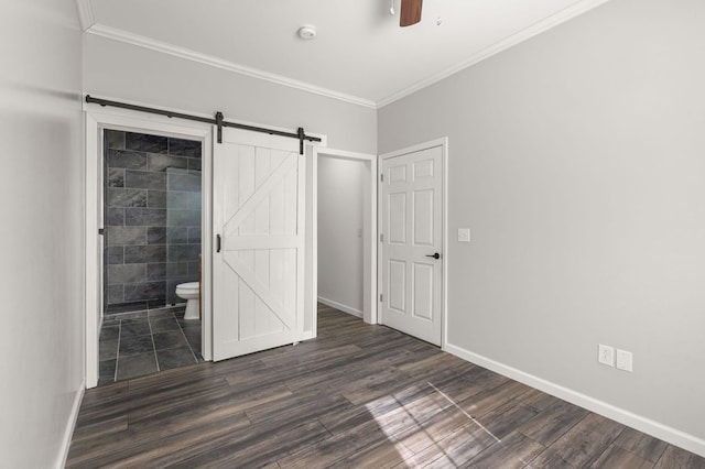 unfurnished bedroom featuring ceiling fan, dark hardwood / wood-style flooring, a barn door, ornamental molding, and ensuite bathroom