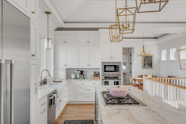 kitchen with built in appliances, sink, a tray ceiling, and hanging light fixtures