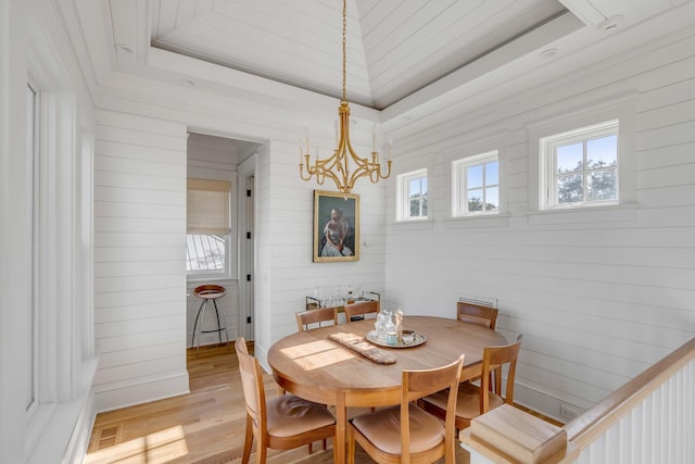 dining area featuring an inviting chandelier, light hardwood / wood-style flooring, and a raised ceiling