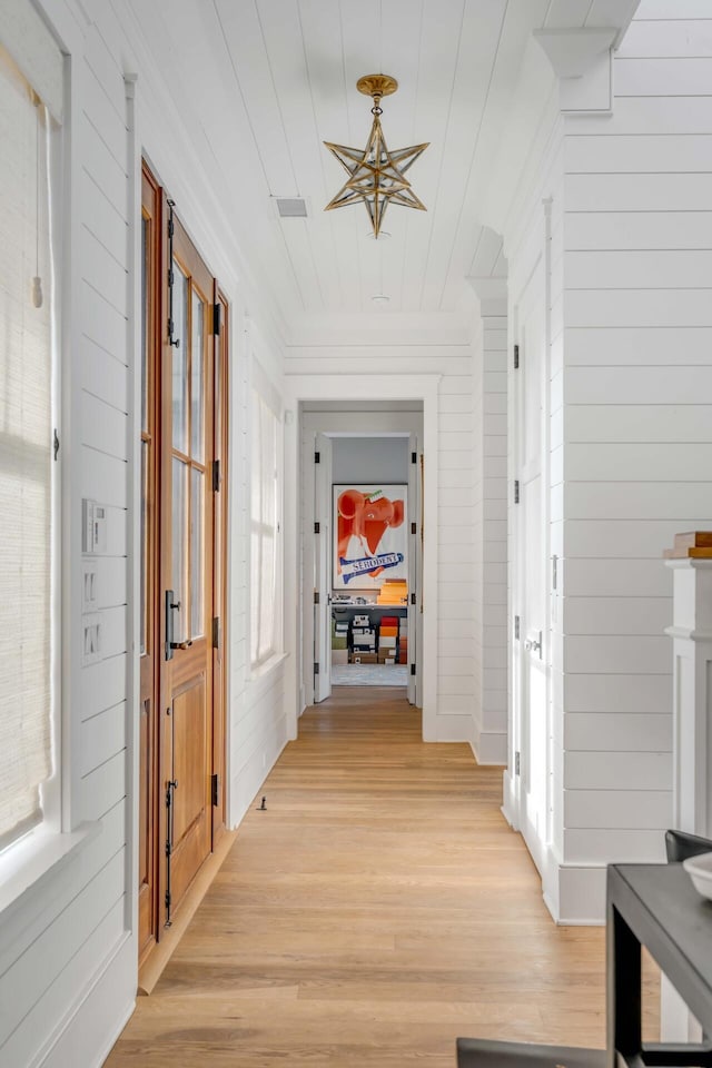 corridor with a wealth of natural light, light hardwood / wood-style floors, and wood walls