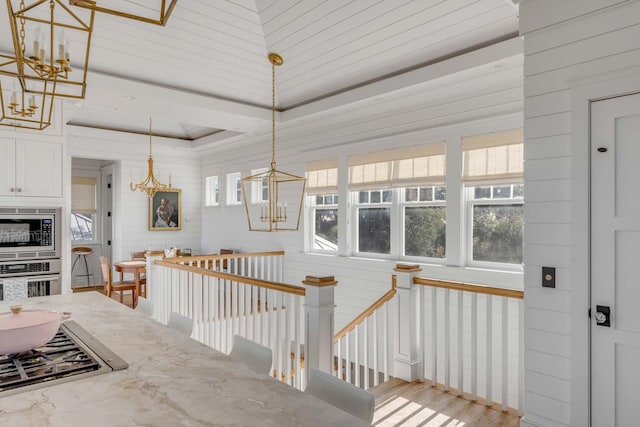 stairs with a raised ceiling, wood-type flooring, and an inviting chandelier