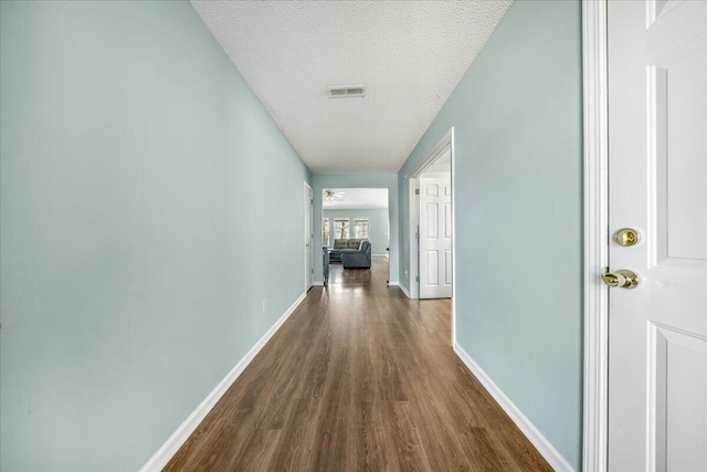 hall featuring visible vents, baseboards, a textured ceiling, and dark wood-style flooring