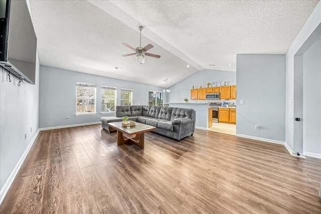 living area featuring baseboards, ceiling fan, vaulted ceiling, light wood-style flooring, and a textured ceiling