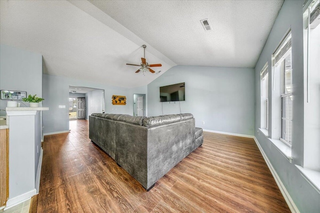 living room featuring visible vents, a ceiling fan, a textured ceiling, wood finished floors, and lofted ceiling