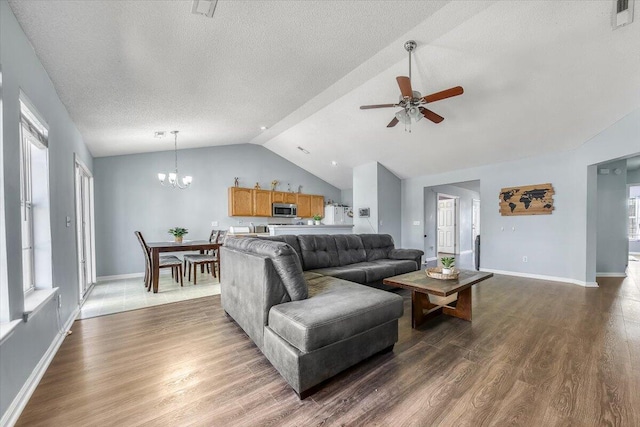 living room with visible vents, ceiling fan with notable chandelier, dark wood-type flooring, and lofted ceiling