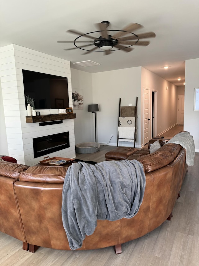 living room featuring a large fireplace, baseboards, a ceiling fan, and light wood-style floors