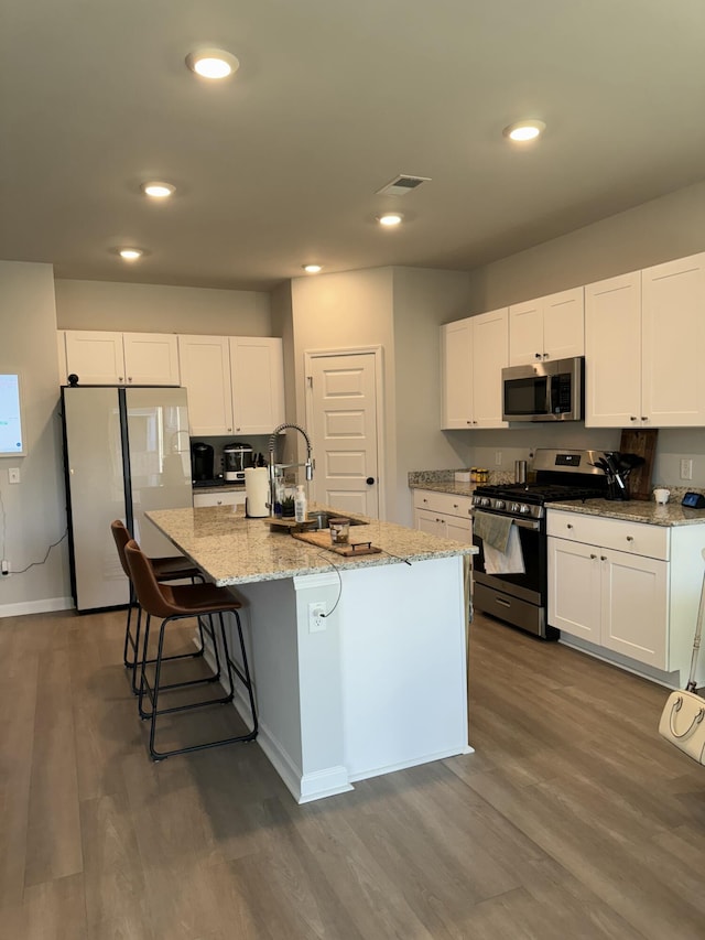 kitchen with a center island with sink, appliances with stainless steel finishes, white cabinets, and a sink