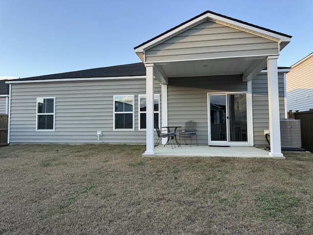 rear view of property with central air condition unit, a patio area, roof with shingles, and a yard