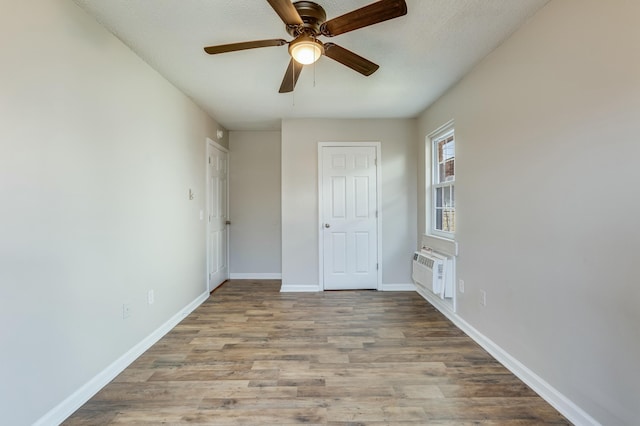 unfurnished bedroom featuring a wall mounted air conditioner, light hardwood / wood-style floors, and ceiling fan