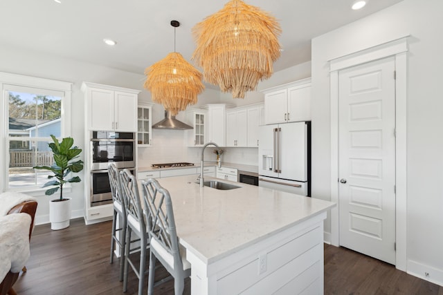 kitchen with appliances with stainless steel finishes, sink, wall chimney range hood, and white cabinets