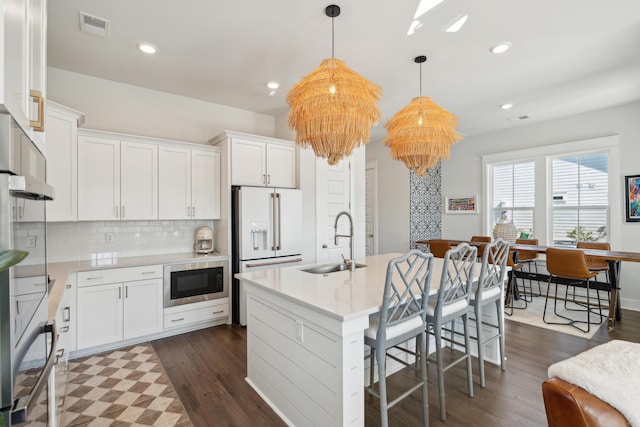 kitchen featuring sink, white cabinetry, hanging light fixtures, an island with sink, and built in microwave