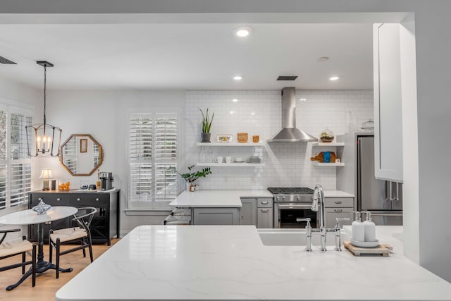 kitchen featuring light wood-type flooring, wall chimney exhaust hood, sink, pendant lighting, and appliances with stainless steel finishes