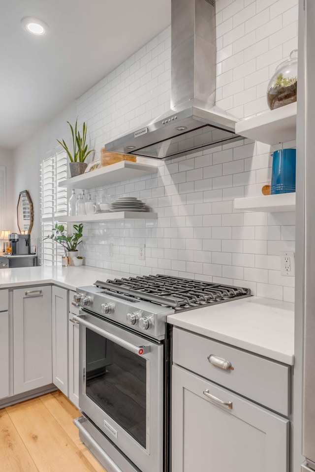 kitchen featuring wall chimney range hood, stainless steel stove, backsplash, and light hardwood / wood-style flooring