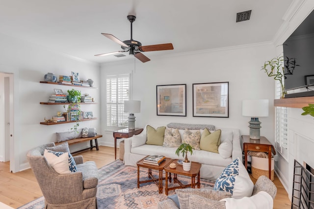 living room with ceiling fan, crown molding, a tiled fireplace, and light hardwood / wood-style flooring