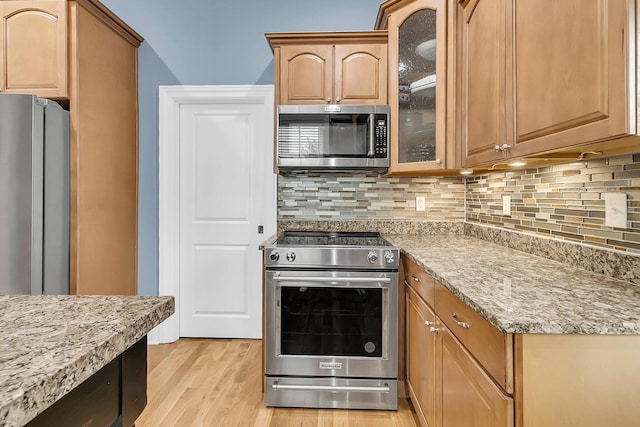 kitchen featuring light stone countertops, appliances with stainless steel finishes, light wood-type flooring, and tasteful backsplash