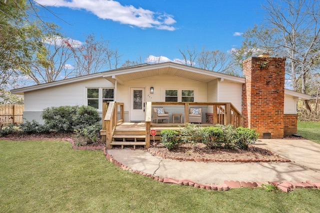 view of front of house with brick siding, fence, a wooden deck, a front yard, and a chimney