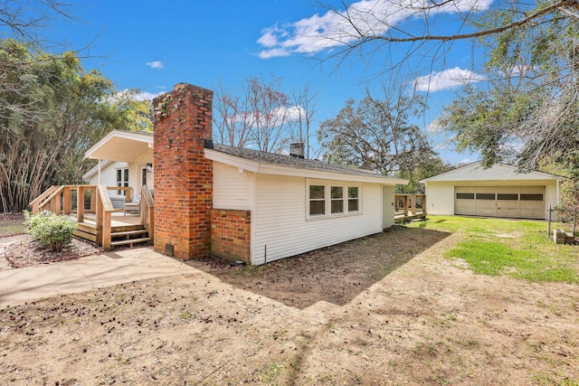 back of house featuring an outbuilding, a chimney, a detached garage, and brick siding