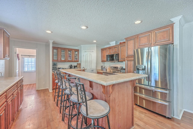 kitchen with a kitchen bar, stainless steel appliances, an island with sink, ornamental molding, and light hardwood / wood-style flooring