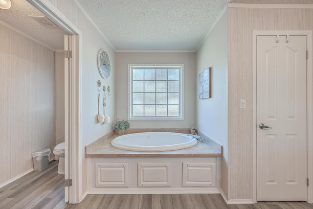 bathroom with toilet, a tub to relax in, crown molding, hardwood / wood-style flooring, and a textured ceiling