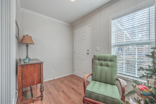 sitting room with plenty of natural light, a textured ceiling, ornamental molding, and light wood-type flooring