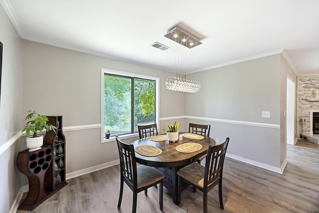 dining area with visible vents, ornamental molding, a stone fireplace, and wood finished floors