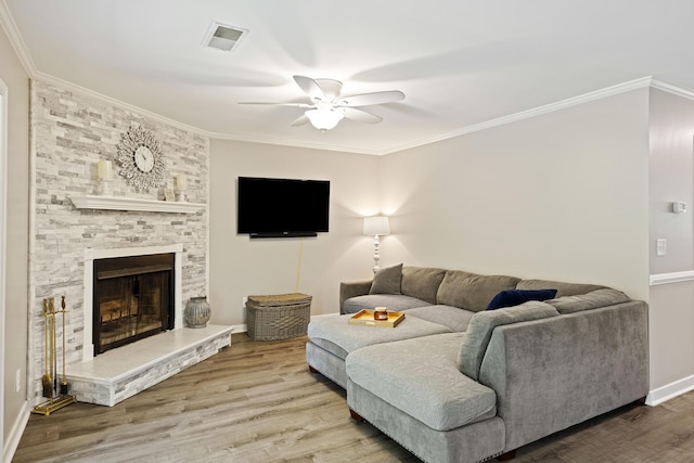 living area featuring visible vents, ornamental molding, a ceiling fan, wood finished floors, and a fireplace