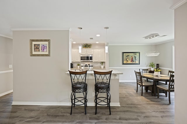 kitchen featuring ornamental molding, stainless steel microwave, white cabinetry, a breakfast bar area, and range