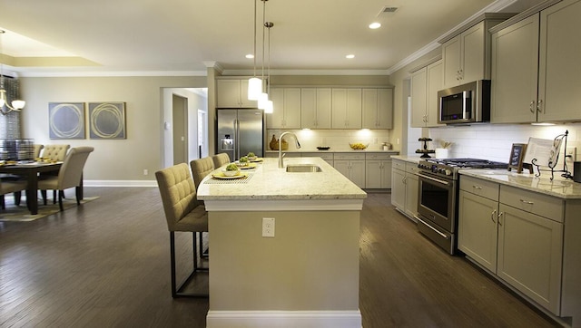 kitchen featuring appliances with stainless steel finishes, sink, hanging light fixtures, a kitchen island with sink, and light stone counters