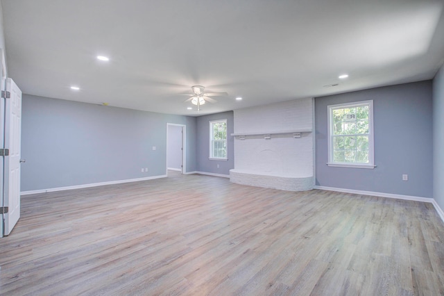 unfurnished room featuring a fireplace, ceiling fan, and light wood-type flooring