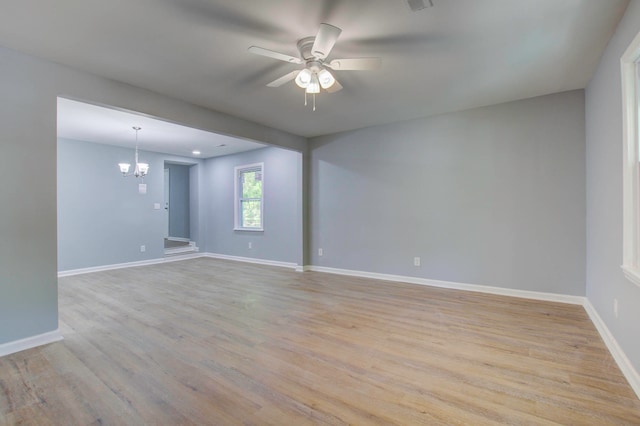 empty room featuring ceiling fan with notable chandelier and light hardwood / wood-style floors