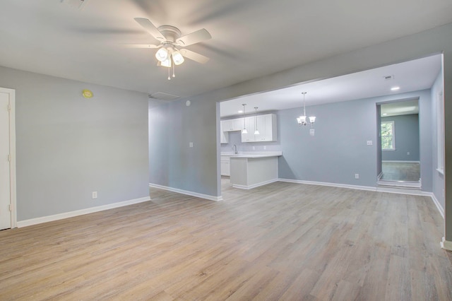 spare room with sink, ceiling fan with notable chandelier, and light wood-type flooring