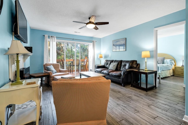 living room with ceiling fan, light wood-type flooring, and a textured ceiling