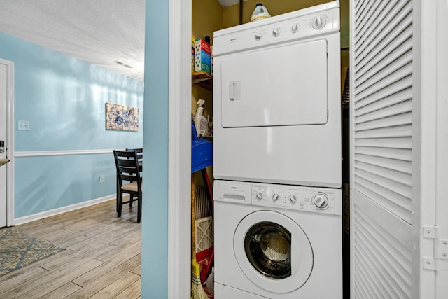 laundry area with stacked washer and clothes dryer, light wood-type flooring, and a textured ceiling