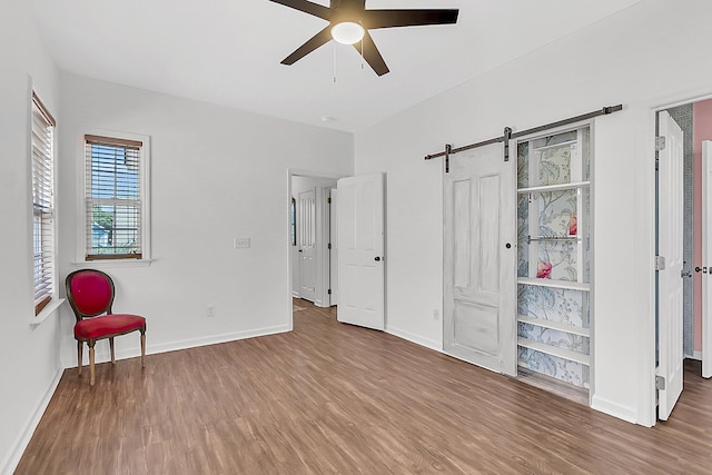 unfurnished bedroom with wood finished floors, a barn door, and baseboards