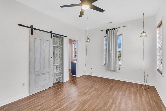 unfurnished bedroom with wood finished floors, baseboards, and a barn door