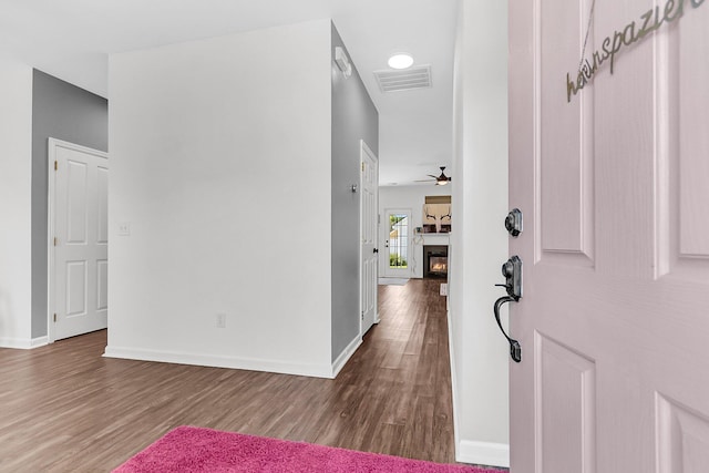 foyer featuring wood finished floors, baseboards, a glass covered fireplace, and a ceiling fan