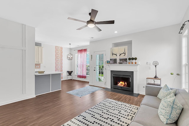 living room featuring dark wood-style flooring, a warm lit fireplace, a ceiling fan, recessed lighting, and baseboards