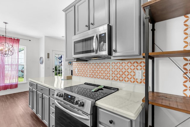 kitchen with appliances with stainless steel finishes, gray cabinetry, tasteful backsplash, dark wood-type flooring, and a chandelier