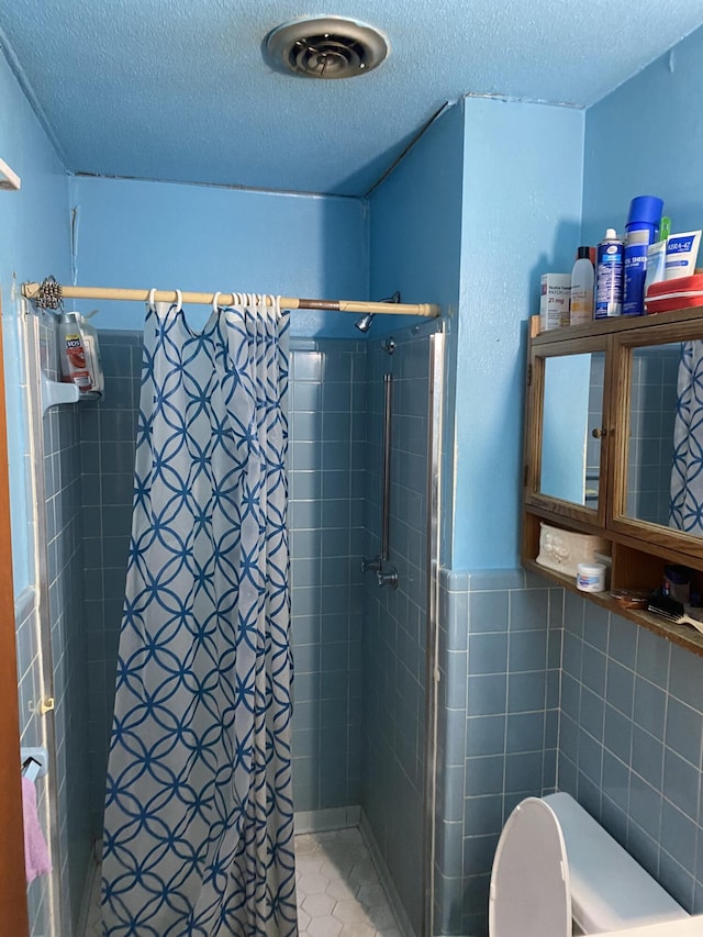 bathroom featuring a shower, a textured ceiling, and tile walls