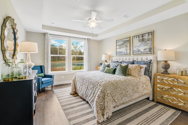 bedroom with a raised ceiling, ceiling fan, and dark wood-type flooring