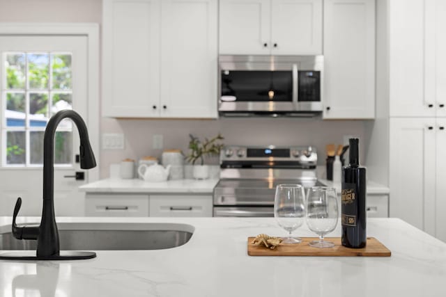 kitchen with appliances with stainless steel finishes, a sink, white cabinetry, and light stone countertops