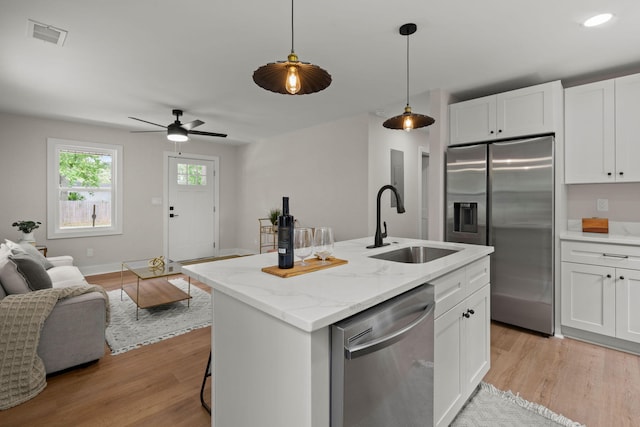 kitchen featuring stainless steel appliances, a sink, open floor plan, light wood-style flooring, and white cabinets