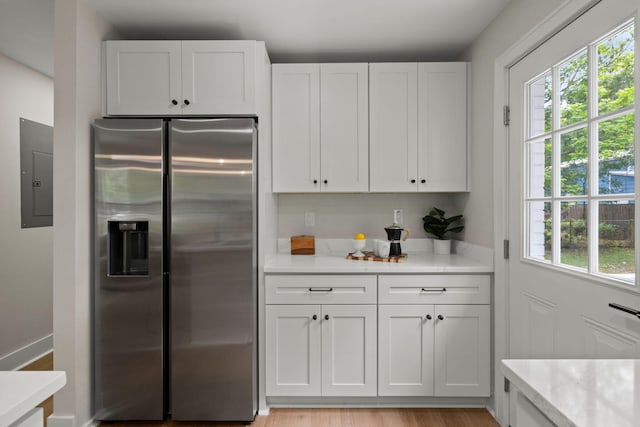 kitchen featuring stainless steel fridge with ice dispenser, electric panel, white cabinets, and light stone counters